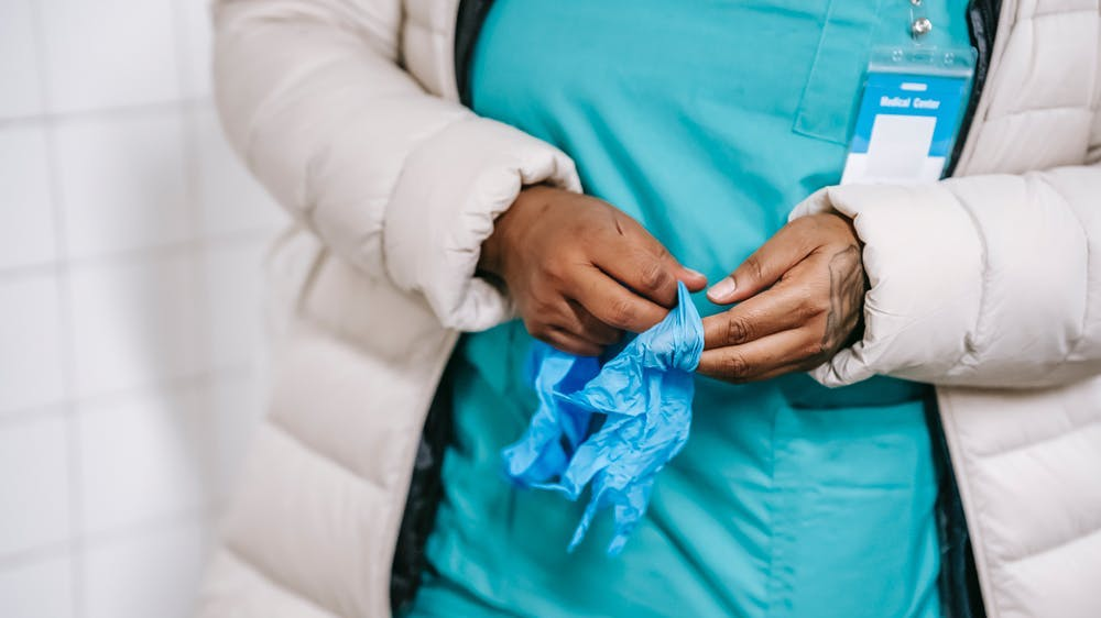 A female nurse wearing a hospital gown is holding a blue bandana in her hand.