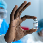 A scientist wearing a white lab coat holds a glass vial containing the coronavirus vaccine