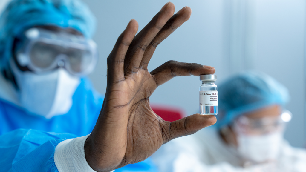 A scientist wearing a white lab coat holds a glass vial containing the coronavirus vaccine